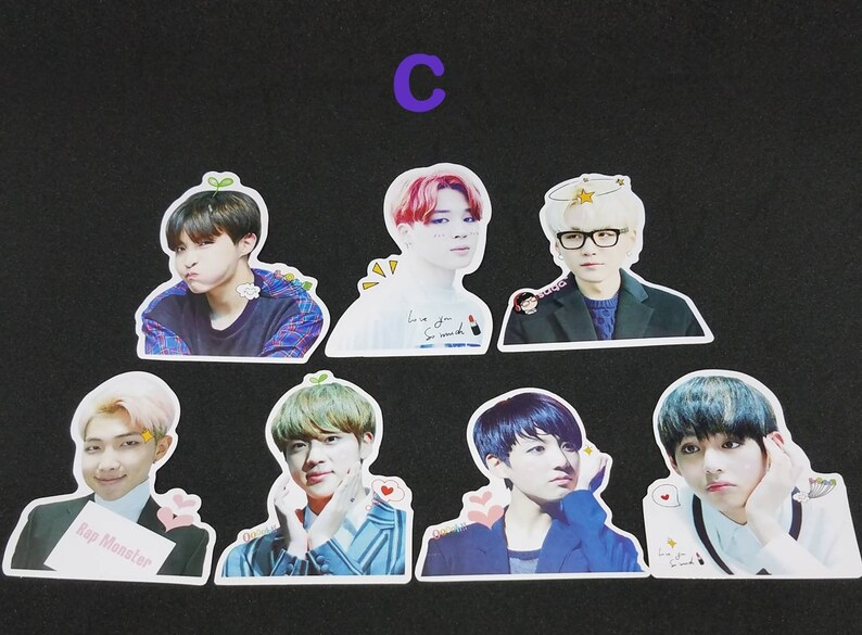 May include: Seven colourful stickers featuring different members of a K-pop band. Each sticker has a white border and features a different member with a unique expression and background. The stickers are printed with the band member's name and a small graphic.