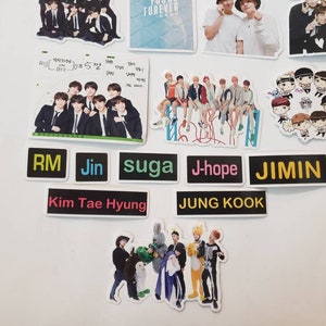 May include: A collection of stickers featuring a K-pop band. The stickers are black and white with colourful text. The text on the stickers reads "RM", "Jin", "suga", "J-hope", "JIMIN", "Kim Tae Hyung", and "JUNG KOOK".