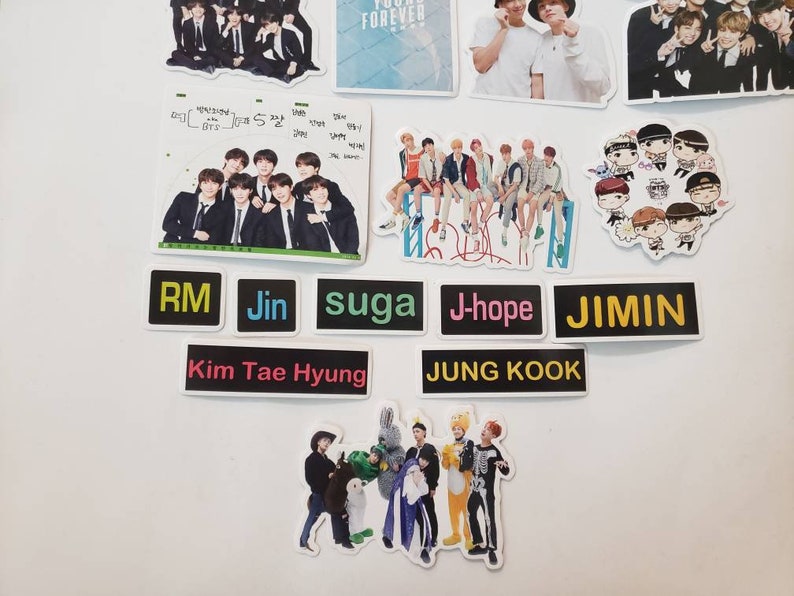 May include: A collection of stickers featuring a K-pop band. The stickers are black and white with colourful text. The text on the stickers reads "RM", "Jin", "suga", "J-hope", "JIMIN", "Kim Tae Hyung", and "JUNG KOOK".