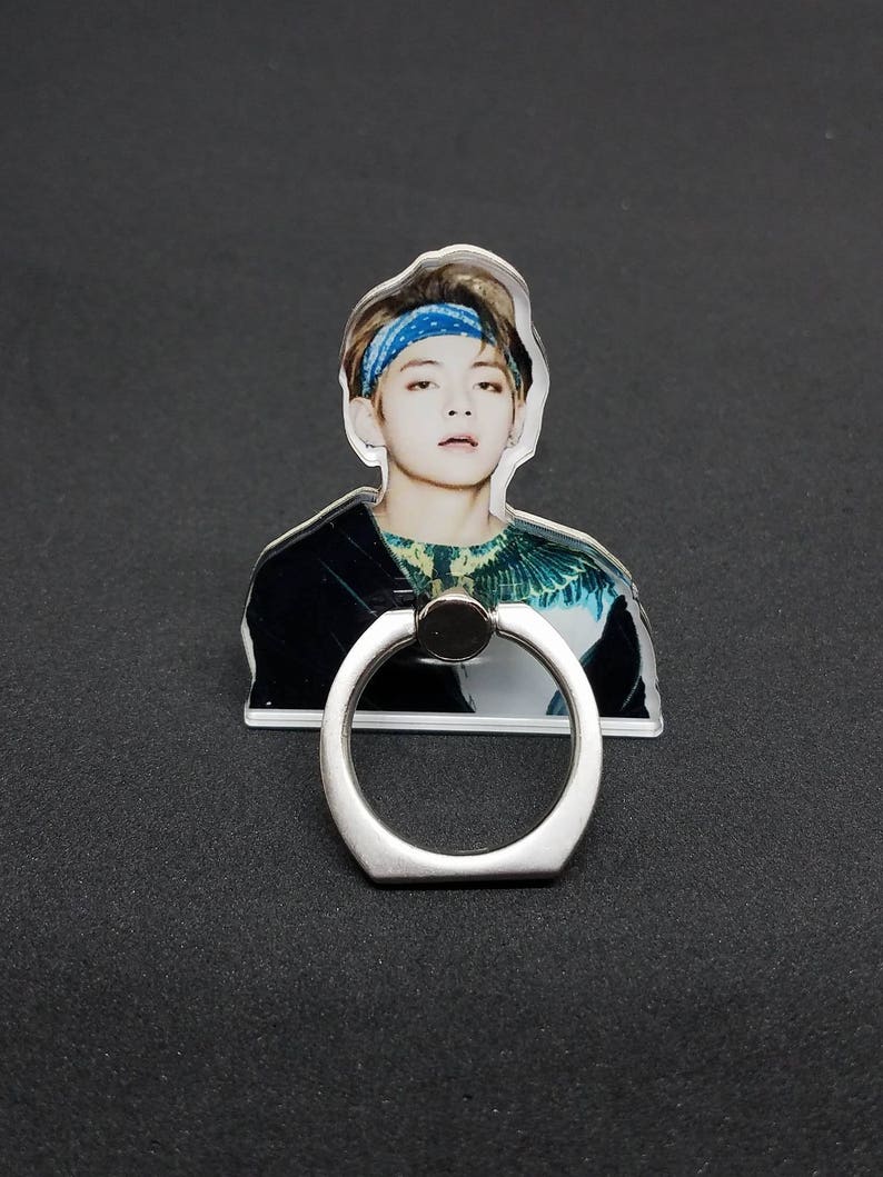 May include: A clear phone ring holder with a silver ring. The holder features a printed image of a person with brown hair wearing a blue bandana and a green and black shirt.