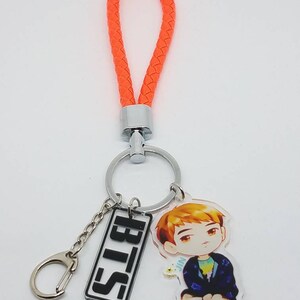 May include: Orange braided keychain with a silver key ring and a charm featuring a cartoon character and the text "BTS".