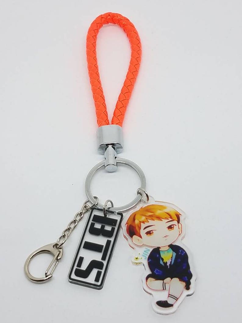 May include: Orange braided keychain with a silver key ring and a charm featuring a cartoon character and the text "BTS".