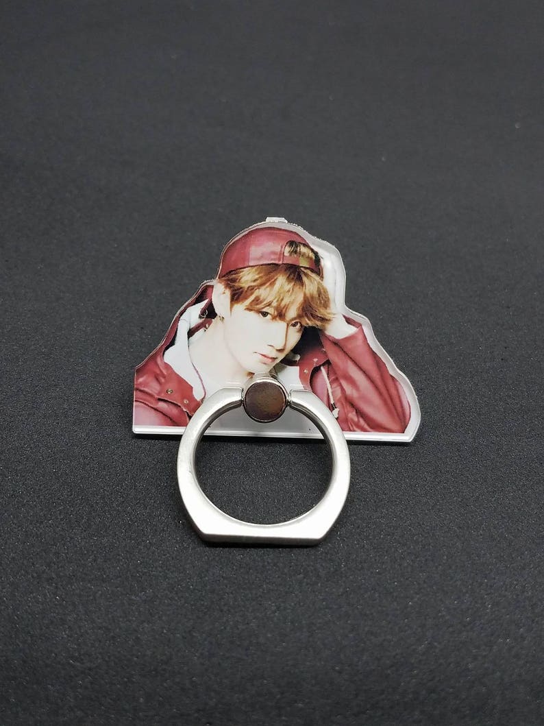 May include: A clear phone ring holder with a silver metal ring. The ring holder features a printed image of a person wearing a red cap and a red jacket.