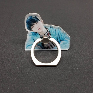 May include: A clear phone ring holder with a photo of a person with blue hair. The ring holder is silver and has a round shape.