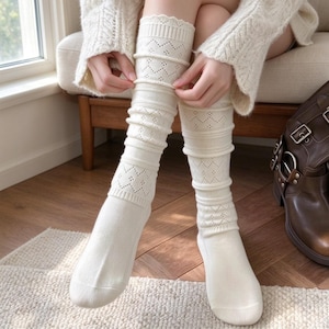 May include: A pair of cream-colored knee-high socks featuring a textured knit pattern with alternating bands of openwork zig-zag designs and solid ribbed sections. The socks have a smooth foot area and a scalloped edge at the top opening.