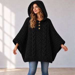 May include: A black crocheted hooded poncho featuring a cable knit pattern on the front, a ribbed hem, and three light brown wooden buttons at the neckline. The garment has a loose, draped fit with wide sleeves and a thick, textured hood.
