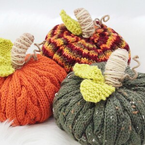 Puede incluir: Tres calabazas de punto en naranja, verde y rojo y marr&oacute;n a rayas. Las calabazas tienen tallos y hojas de ganchillo.