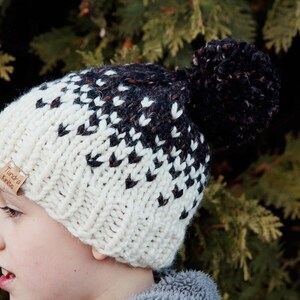 May include: A white and black knit hat with a brown pom pom. The hat has a label that says "Tundra Knits".