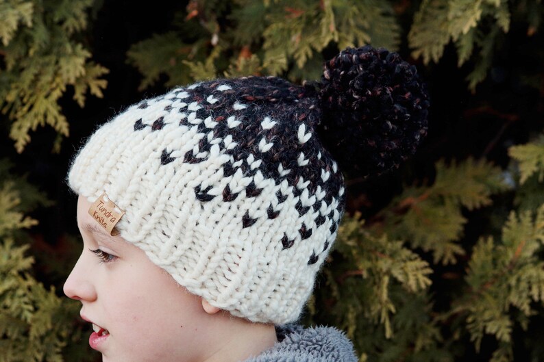 May include: A white and black knit hat with a brown pom pom. The hat has a label that says "Tundra Knits".