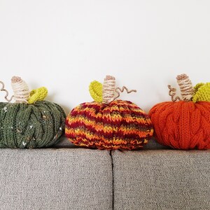 Puede incluir: Tres calabazas de punto en verde, naranja y rojo y amarillo a rayas. Las calabazas est&aacute;n sentadas en un sof&aacute; gris.