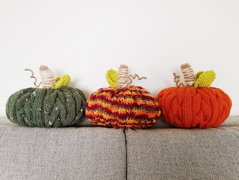 Puede incluir: Tres calabazas de punto en verde, naranja y rojo y amarillo a rayas. Las calabazas est&aacute;n sentadas en un sof&aacute; gris.