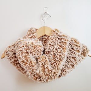 May include: A fluffy brown and white faux fur neck warmer hanging on a wooden hanger.