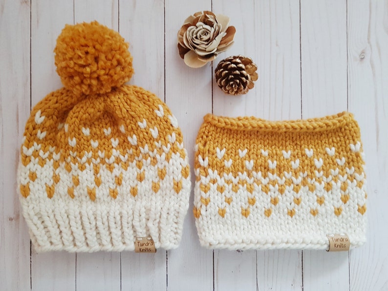 May include: A yellow and white knit hat with a pom pom on top and a matching knit neck warmer. Both items have a geometric pattern and a brown tag that says "Tundra Knits".