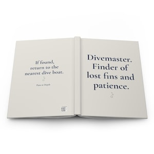 May include: An open book with off-white pages and dark blue text. The left page reads: If found, return to the nearest dive boat. Puns at Depth. The right page reads: Divemaster. Finder of lost fins and patience. Small bubble icons are present.