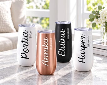 May include: Four stemless tumblers with clear lids, featuring custom names and titles in script font. Two are white with black text reading Portia Bride and Harper Bridesmaid, one is rose gold with white text Annika Bridesmaid, and one is black with white text Elaina Bridesmaid.