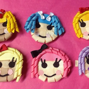May include: Six handmade ribbon doll faces with curly hair and bows. Each face is made of woven ribbons in various colors, including yellow, blue, pink, and purple. The faces have black eyes, smiles, and blush, set against a pink background.