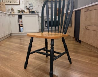 May include: A wooden chair featuring a black spindle back and frame with a natural light brown wood seat. The chair has four turned legs connected by horizontal stretchers and a curved top rail, showcasing a two-tone finish throughout.