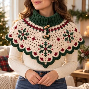 May include: A cream-coloured crochet capelet featuring a dark green ribbed collar, two wooden toggle buttons, and a repeating pattern of dark green snowflakes and small red star accents. The hem has a scalloped dark green crochet edge.