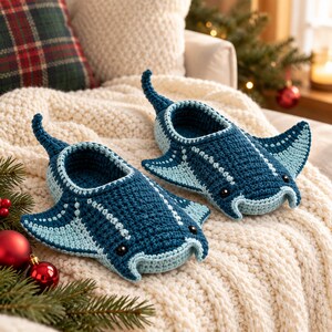 May include: A pair of crochet slippers shaped like manta rays in dark blue and light blue yarn. The slippers feature small black bead eyes, wide side fins, and a pointed tail extending from the back of each heel opening.