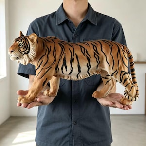 Pode incluir: Uma estatueta de tigre com uma pelagem realista de listras laranjas e pretas, barriga branca e características faciais detalhadas, incluindo orelhas pontudas e uma juba texturizada. A escultura é retratada em pé, de perfil.