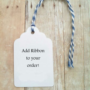 May include: White gift tag with scalloped edges and blue and white twine. The tag says "Add Ribbon to your order!"