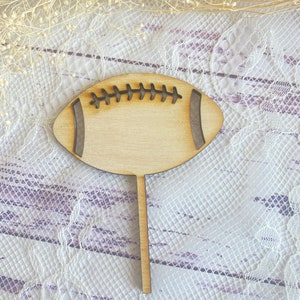 Pu&ograve; includere: Sagoma di legno di un pallone da calcio con un design cucito. Il pallone da calcio &egrave; su un bastone ed &egrave; pronto per essere utilizzato come topper per torte.