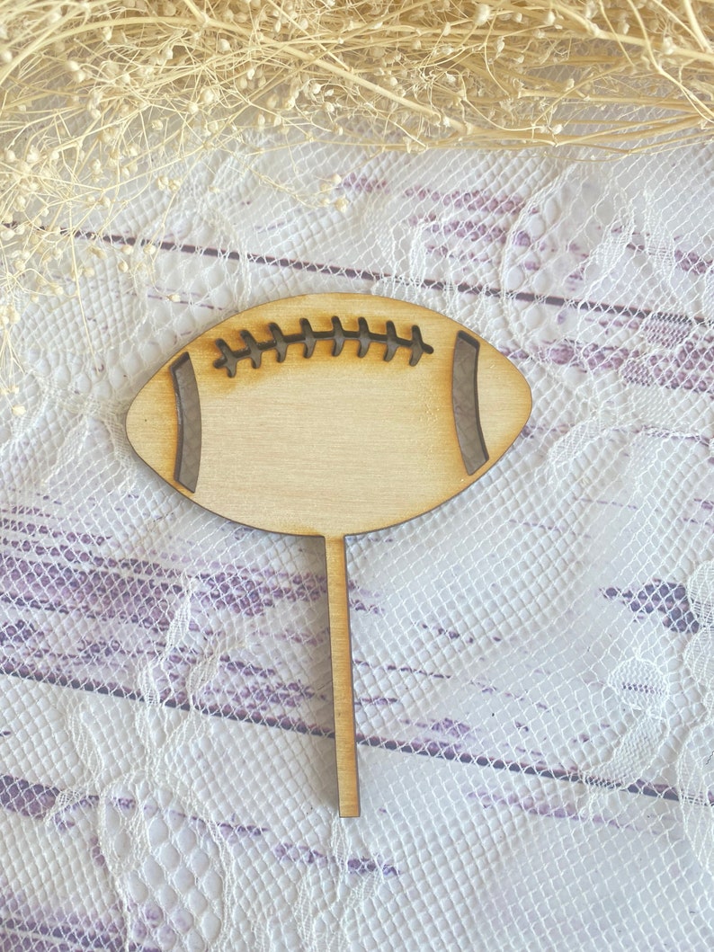 Pu&ograve; includere: Sagoma di legno di un pallone da calcio con un design cucito. Il pallone da calcio &egrave; su un bastone ed &egrave; pronto per essere utilizzato come topper per torte.