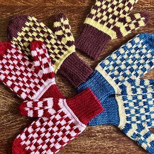 May include: A collection of five knitted mittens featuring checkered patterns in various color combinations including maroon and yellow, red and light pink, and blue and cream. Each mitten has a solid ribbed cuff matching the primary color.