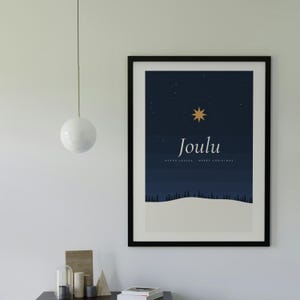 May include: A framed wall art print featuring a dark blue night sky with a golden star, a snowy landscape with a dark forest silhouette, and the text "Joulu", "Hyvää Joulua", and "Merry Christmas" in white lettering.