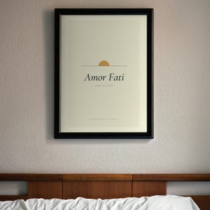 Puede incluir: Una lámina enmarcada con fondo crema, una línea horizontal fina y un semicírculo dorado. El texto dice Amor Fati, Love of Fate y To want nothing to be different en una fuente serif negra dentro de un marco de color negro.