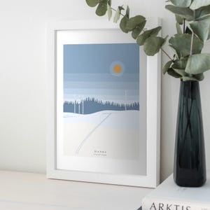 May include: A framed art print featuring a stylised winter landscape with a blue sky, a yellow sun, a dark blue forest, and snow-covered ground. The print includes the text HANKI DEEP SNOW in the lower centre area of the composition.