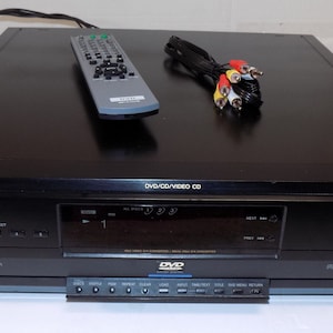 May include: Black Sony DVD/CD player with a remote control and AV cables. The player has a sleek design with buttons for disc selection and playback. The remote is gray and the AV cables have red, white, and yellow connectors.