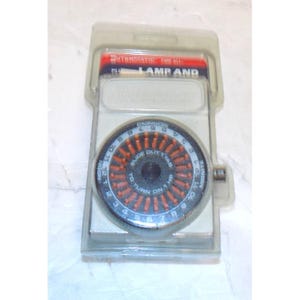 May include: A new Intermatic lamp timer in its original packaging. The timer has a black and orange dial with numbers and the words "MORNING" and "MIDNITE". The packaging is clear plastic with red and black text.