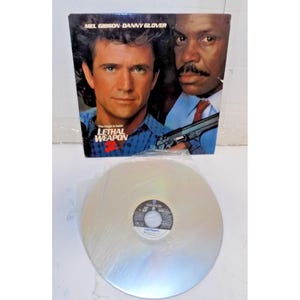 May include: A vintage "Lethal Weapon 2" movie LaserDisc with Mel Gibson and Danny Glover on the cover. The disc is silver and in a plastic sleeve. The movie title is displayed in blue and red.