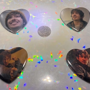 May include: Four heart-shaped badges featuring photographic portraits of a person. The badges are arranged around a central coin. Each badge displays a different image of the same individual in various settings and facial expressions.
