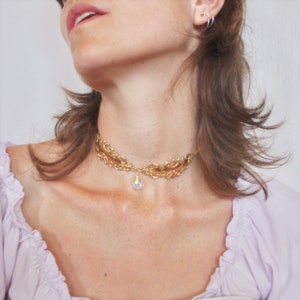 May include: A gold-tone choker necklace with a delicate, ornate design and a dangling iridescent crystal pendant.