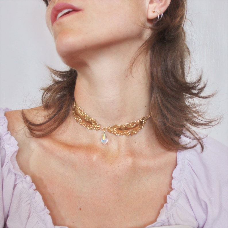May include: A gold-tone choker necklace with a delicate, ornate design and a dangling iridescent crystal pendant.