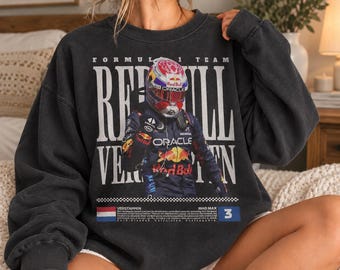 May include: A charcoal gray crewneck sweatshirt featuring a graphic of a Formula 1 driver in a racing suit and helmet. The text reads Formula 1 Team Red Bull, Oracle, Verstappen, and Mad Max, with a Dutch flag and the number 3 displayed.