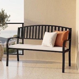 May include: A black metal outdoor bench featuring a curved backrest with vertical slats, a long white seat cushion, and two decorative throw pillows in solid white and burnt orange colors, positioned on a balcony with a view.