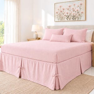 May include: A light pink bed set featuring a fitted sheet, two standard pillows, and one rectangular bolster pillow. The bed is finished with a matching pink bed skirt that includes decorative tie-knot details at each corner pleat.