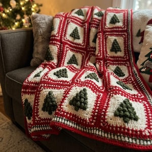 May include: A handmade crochet blanket featuring a repeating pattern of square blocks. Each square contains a textured, dark green bobble-stitch Christmas tree centered on a cream-colored background, framed by vibrant red yarn borders.