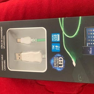 Peut inclure: Une boîte rectangulaire noire pour un câble de charge Grundig. La boîte présente une fenêtre transparente montrant un connecteur micro USB blanc et un connecteur USB-A blanc. L'emballage indique une longueur de 1 mètre et une LED lumineuse.