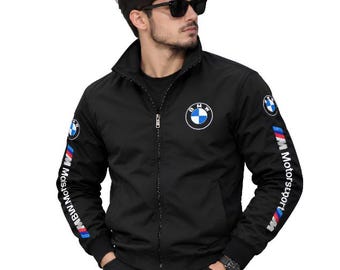 Peut inclure: Une veste noire zippée avec un col montant et des manches longues. La poitrine arbore un logo BMW circulaire. Les deux manches sont ornées du logo BMW et du texte BMW Motorsport en blanc, avec des bandes bleues et rouges.