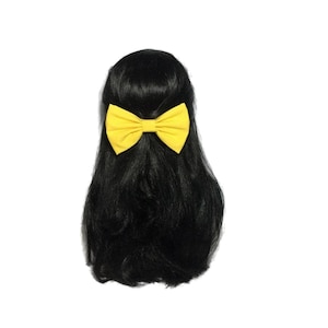 May include: A yellow fabric bow tied in a hair clip. The bow is on a black wig.
