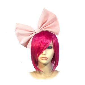 May include: A large pink fabric bow headband. The headband is worn on a mannequin with short, bright pink hair.