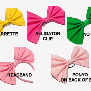 May include: Five fabric bows in different colours with different ways to attach them.  The bows are yellow, pink, green, light pink, and light pink.  The yellow bow has a barrette clip, the pink bow has an alligator clip, the green bow has no clip, the light pink bow has a headband, and the other light pink bow has a ponyo on the back of the bow.