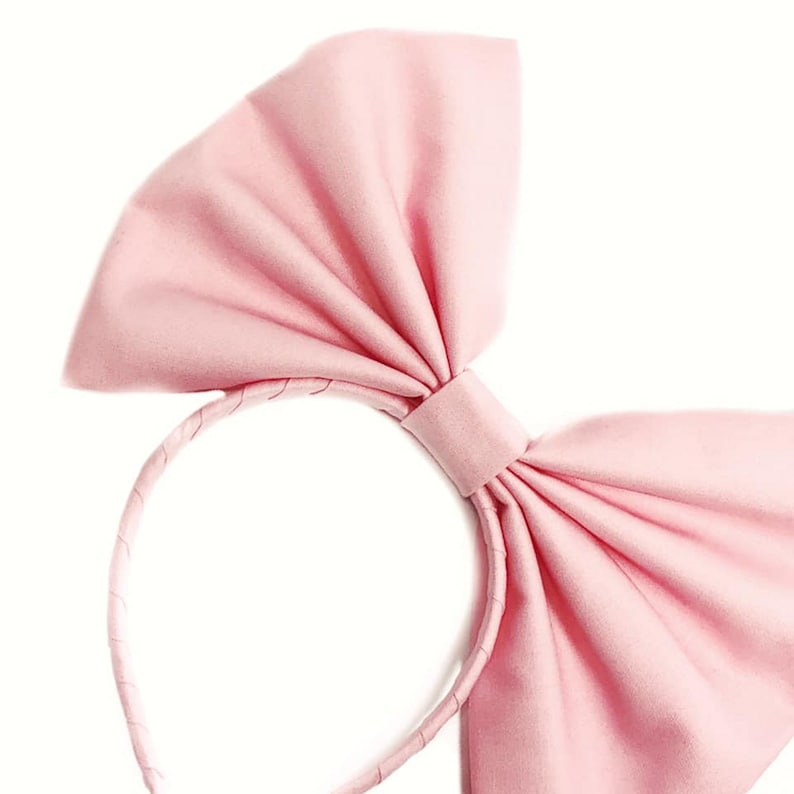May include: A pink fabric headband with a large bow. The headband is made of a soft, flexible material and is perfect for adding a touch of elegance to any outfit.