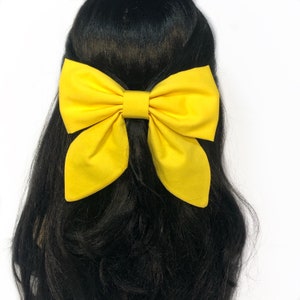 May include: A large yellow bow made of fabric is worn in the hair of a person with long black hair.