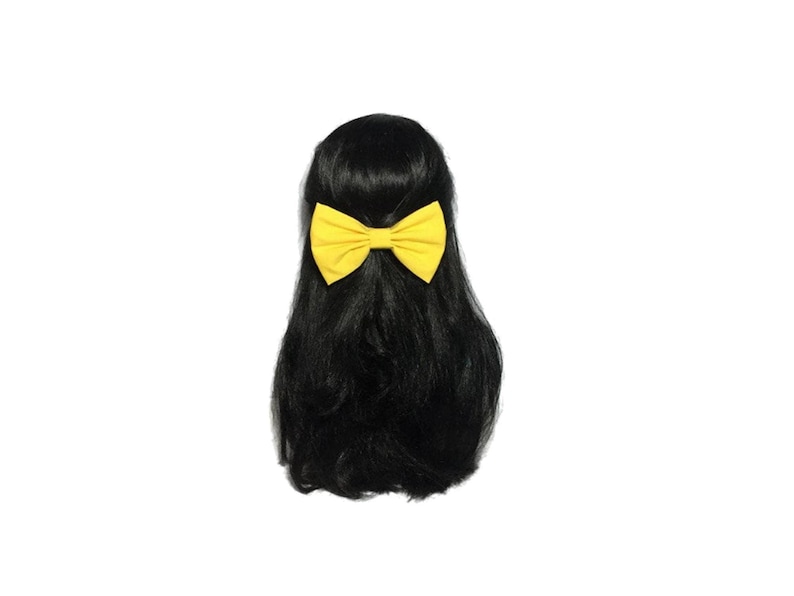 May include: A yellow fabric bow tied in a hair clip. The bow is on a black wig.