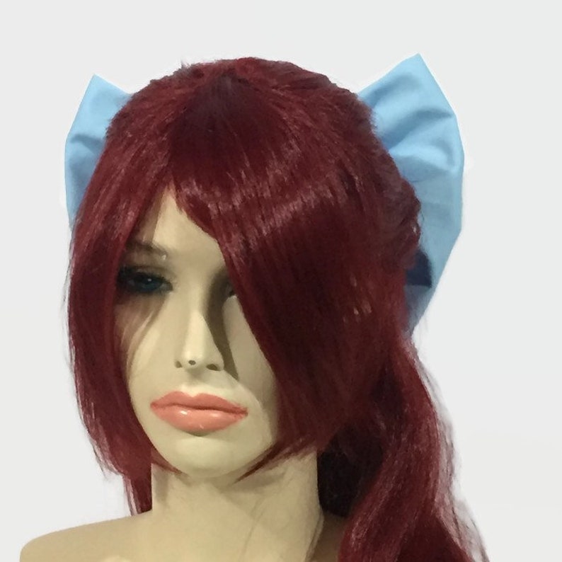 May include: A light blue fabric headband with a bow on each side. The headband is worn on a mannequin with long, red hair.